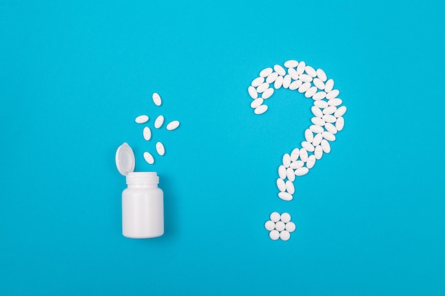 Znak Zapytania Wykonany Z Białych Pigułek I Tabletek Z Pojemnikiem Na Pigułki Leżącym Na Niebieskim Tle światowy Przemysł Farmaceutyczny I Produkty Lecznicze