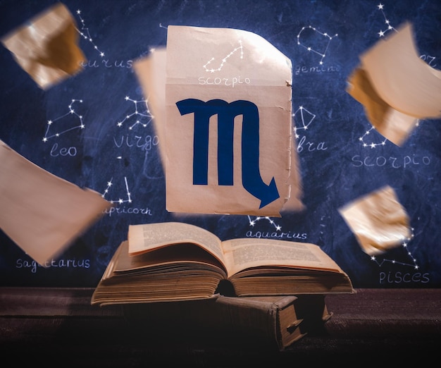 Zdjęcie znak zodiaku skorpion na starym papierze latający nad starymi książkami astrologicznymi