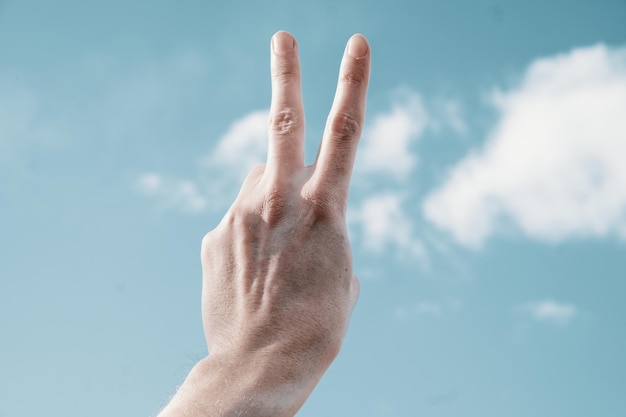 Zdjęcie znak zwycięstwa palcami dłoni na tle błękitnego nieba. dwa palce uniesione do góry na tle nieba.