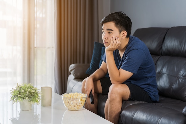 Znudzony człowiek ogląda telewizję i siedzi na kanapie w salonie