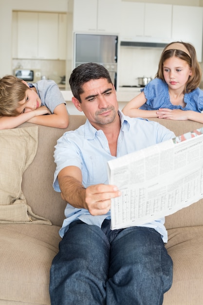 Znudzony dzieci patrząc na czytanie gazety ojca w domu