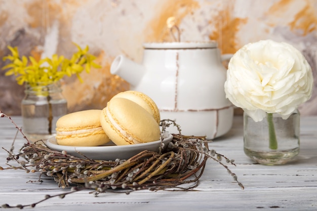 Żółci macaroons w gniazdeczku i kwiatach na białym rocznika drewnie