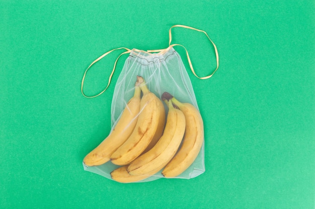 Żółci świezi banany w eco naturalnych torbach szy od siatki płótna na zielonym tle z kopii przestrzenią