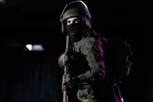 Żołnierz armii w mundurach bojowych z karabinem szturmowym i hełmem bojowym w nocnej misji na ciemnym tle. Niebieski i fioletowy efekt świetlny żelu. Zdjęcie wysokiej jakości