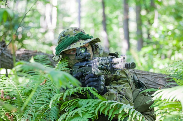 Żołnierz w lesie siedzi w zasadzce. Karabin maszynowy i ubranie żołnierza