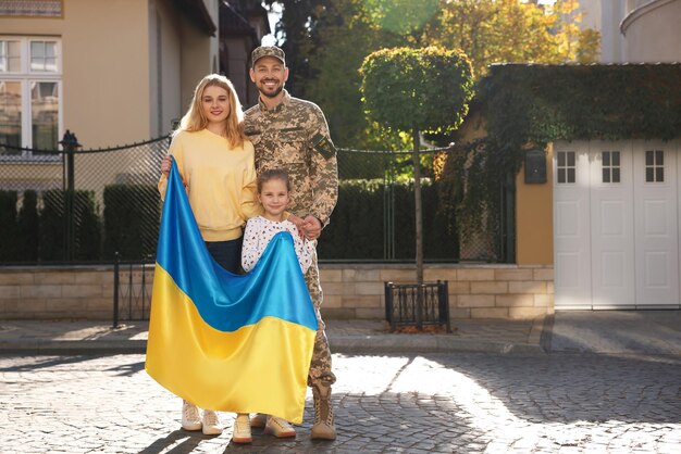 Żołnierz w mundurze wojskowym ponownie połączył się z rodziną i ukraińską flagą na ulicy miasta dla tekstu