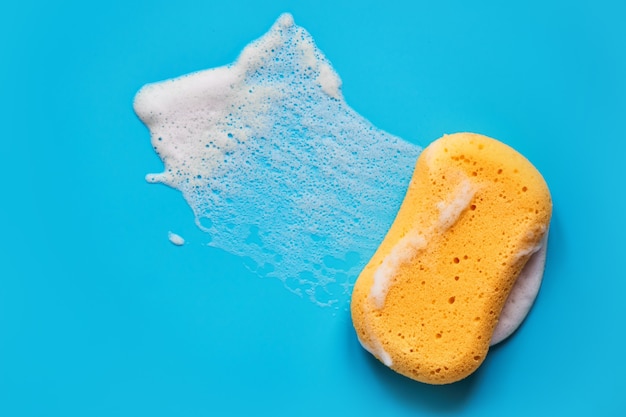 Zdjęcie Żółta gąbka do mycia w piance mydlanej na niebieskim tle na białym tle