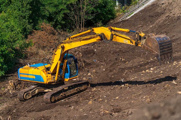 Żółta koparko-ładowarka z hydraulicznym ramieniem tłokowym na jasne, błękitne niebo. Ciężka maszyna do wykopów na budowie. Maszyny hydrauliczne. Ogromny spychacz. Przemysł maszynowy ciężki. Inżynieria mechaniczna.