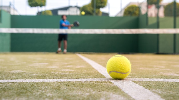 Żółta piłka na podłodze za siatką do wiosłowania na zielonym korcie na zewnątrz Padel tenis