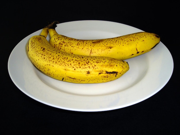 Żółte banany na białym talerzu na czarnym tle
