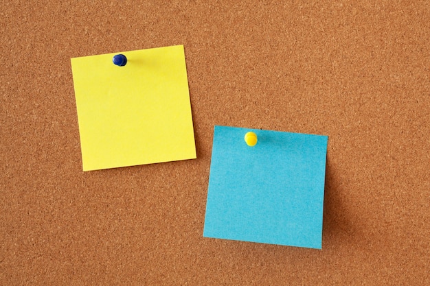 Żółte i niebieskie kartki na notatki na tablicy korkowej. Powierzchnia biurowa lub biznesowa.