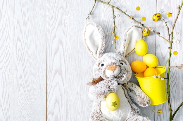 Zdjęcie Żółte i pomarańczowe pisanki wielkanocne malowane jaja kurze w wiaderku wystrój z króliczkiem zabawki gałęzie wierzby wiosna koncepcja wielkanocna na drewnianym tle chrześcijańskie prawosławne wakacje