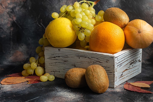 Żółte jabłka kiwi z pomarańczowymi winogronami w białym drewnianym pudełku Jesienny zestaw owoców