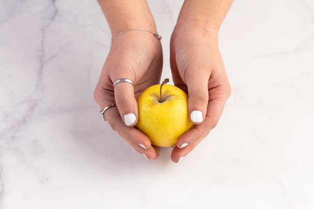 Żółte jabłko w rękach na powierzchni marmuru