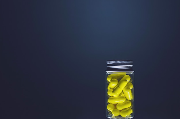 Żółte kapsułki w przezroczystej szklanej butelce średniej wielkości, odizolowanej na ciemnym tle. Naturalne suplementy dla zdrowia. Oświetlenie studyjne.