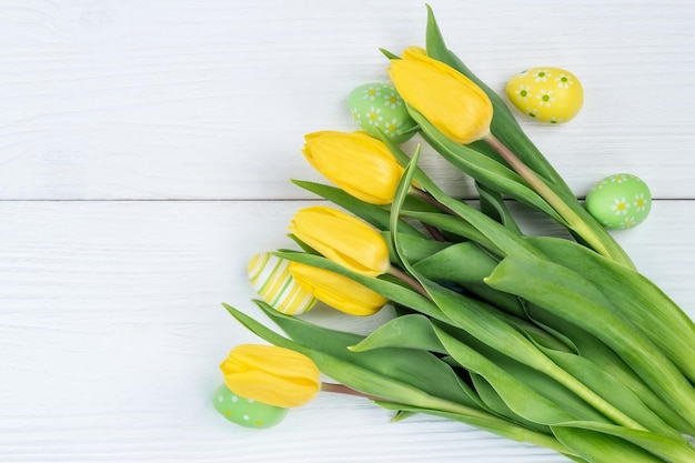 Żółte tulipany i jaja wielkanocne na białym drewnianym stole