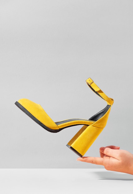 Żółte zamszowe buty na wysokim obcasie balansujące na palcu kobiecej dłoni.