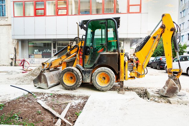 Żółty ciągnik z przednimi i tylnymi wiadrami hydraulicznymi stoi na placu budowy w mieście