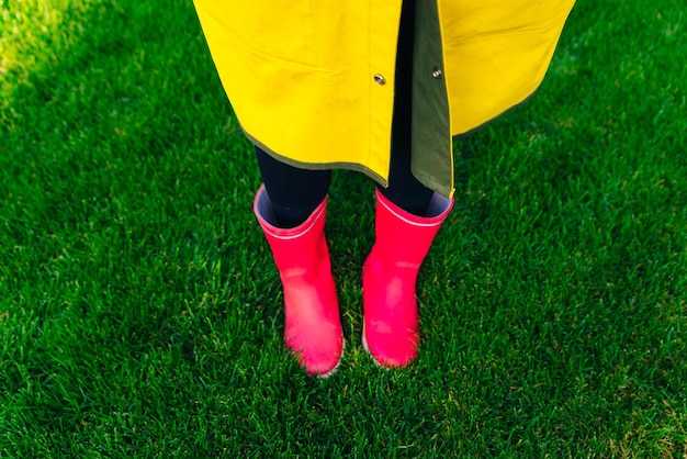 Żółty płaszcz przeciwdeszczowy Gumowe różowe buty przeciw Konceptualnemu wizerunkowi nóg w butach na zielonej trawie
