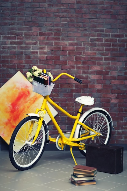 Żółty rower z książkami na tle ściany z cegły