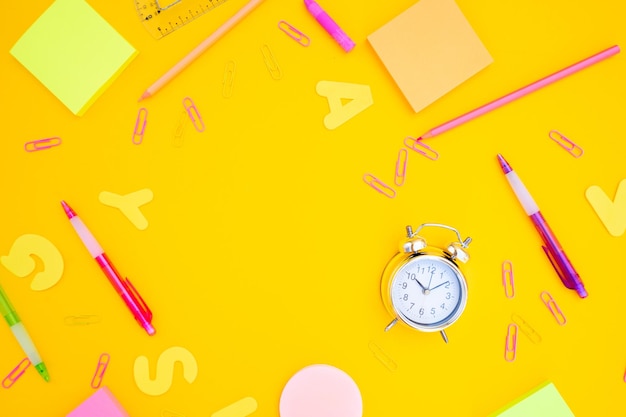 żółty stół z zegarem, ołówkami i ołówkiem.