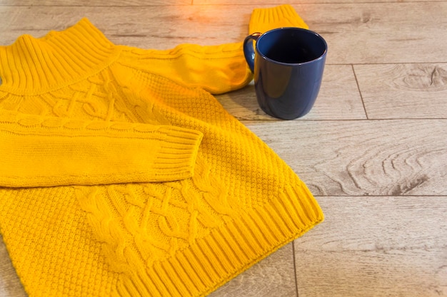 Żółty sweter na szarym drewnianym tle obok niebieskiego kubka gorącego napoju