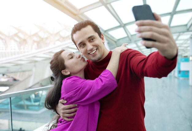 Żona całuje męża robi selfie na telefonie przy lotniskiem