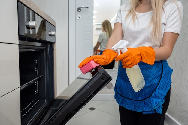 Żona w pomarańczowych rękawiczkach do czyszczenia drzwi piekarnika w jej koncepcji dezynfekcji prac domowych