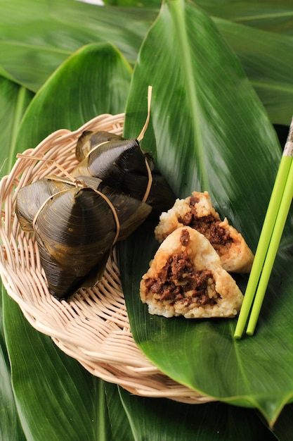 Zongzi lub Bakcang (Bacang). Chińskie pikantne knedle z ryżem kleistym w opakowaniu z liści bambusa. Podawany na talerzu rattanowym. Pokrojone na pół i pokazane mięso (wieprzowina, kurczak, wołowina) w środku.