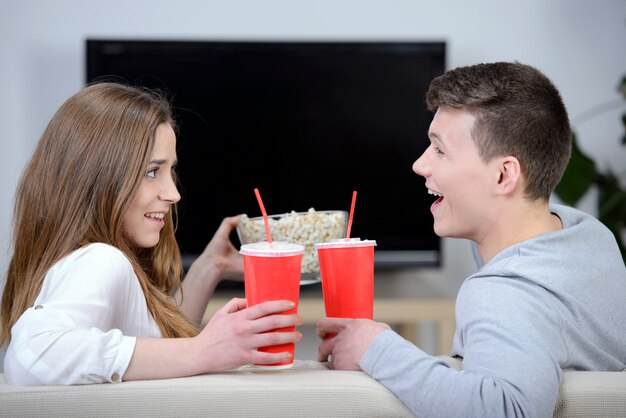 Zrelaksowana młoda para ogląda telewizję i pije koli.