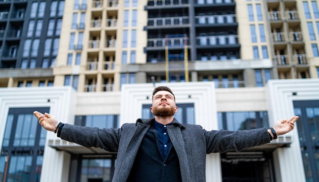 Zrelaksowany mężczyzna stojący z otwartymi ramionami w pobliżu nowoczesnego budynku Podekscytowany biznesmen nie może się doczekać nowych celów