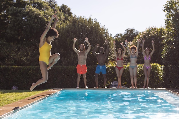 Zróżnicowana grupa przyjaciół bawiących się i skaczących do wody na imprezie przy basenie. Latem spędzać czas i relaksować się na świeżym powietrzu.