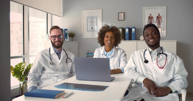 Zróżnicowani koledzy medyczni siedzący przy biurku, rozmawiający i śmiejący się w biurze kliniki