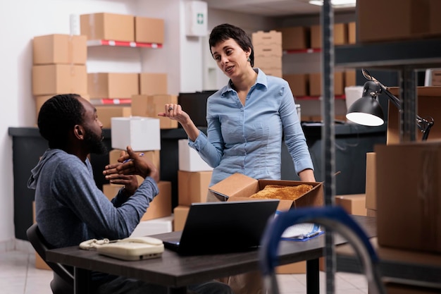Zróżnicowani pracownicy omawiają logistykę transportu podczas przygotowywania paczek, składając zamówienie klienta w kartonowym pudełku podczas zmiany pracy. Zespół pracujący w dziale dostaw w magazynie