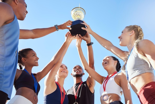 Zdjęcie zróżnicowany zespół sportowców świętujących zwycięstwo ze złotym trofeum i wyglądających na podekscytowanych zgrany i szczęśliwy zespół profesjonalnych sportowców radujących się po wygraniu nagrody na imprezie sportowej