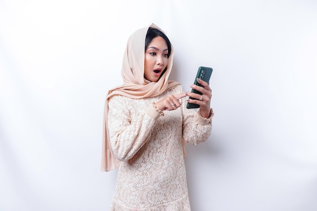 Zszokowana azjatycka kobieta ubrana w hidżab trzymająca telefon odizolowany białym tłem
