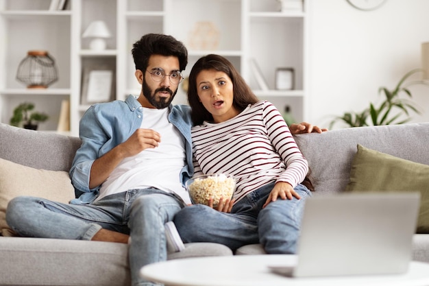 Zszokowana para ze Wschodu oglądająca telewizję razem w domu