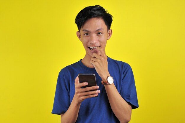 Zszokowana twarz azjatyckiego człowieka w białej koszuli, patrząc na ekran telefonu na żółtym tle.
