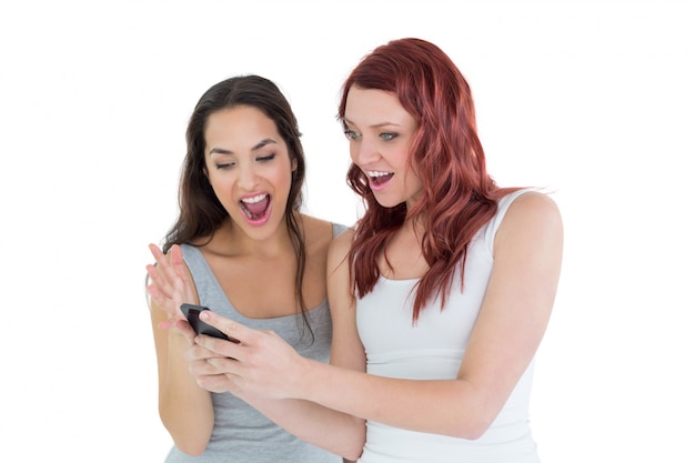 Zszokowani żeńscy przyjaciele patrzeje telefon komórkowego