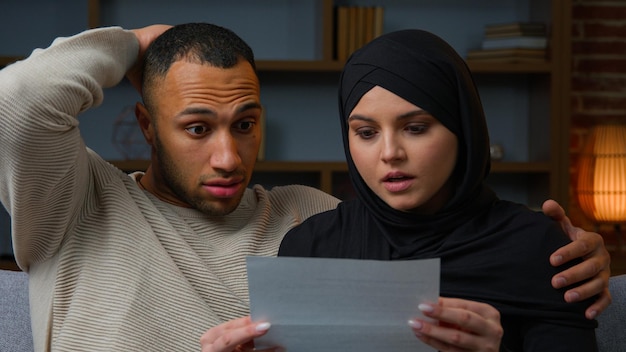 Zszokowany afrykański mąż latynoski z arabską muzułmańską żoną otwierającą kopertę i czytającą