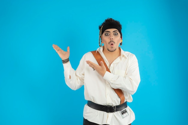 Zszokowany przystojny pirat stoi na niebieskim tle i wskazuje ręce na prawą stronę. Zdjęcie wysokiej jakości