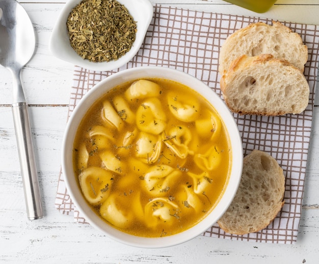 Zupa cappelletti lub tortellini brodo w misce z kromkami chleba i przyprawami na drewnianym stole