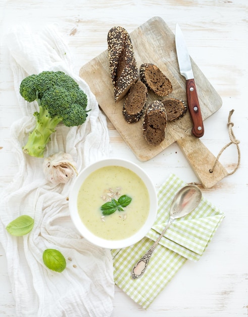 Zupa krem brokułowy z pestkami słonecznika świeżą bazylią i chlebem w misce na białym drewnianym stole