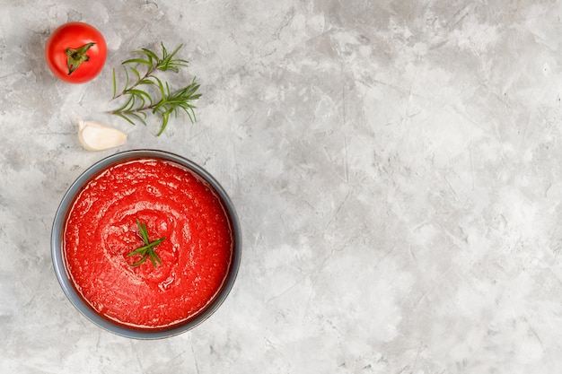 Zupa pomidorowa w misce ozdobionej rozmarynem z pomidorami i czosnkiem na szarej kamiennej ścianie