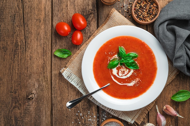 Zupa pomidorowa ze śmietaną i listkami bazylii na drewnianym tle