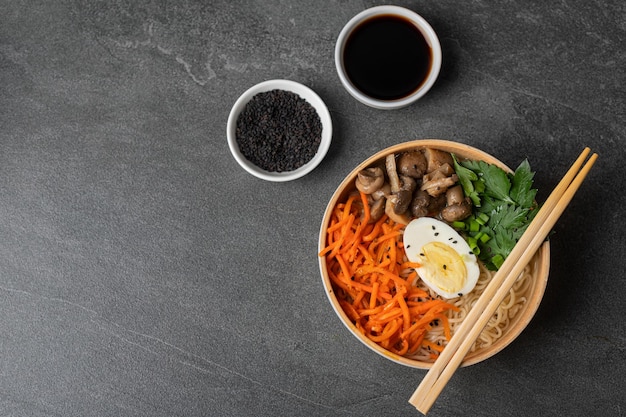 Zupa z makaronem ramen w białej misce z jajkiem kurzym, marchewką, grzybami na ciemnym tle kamienia łupkowego