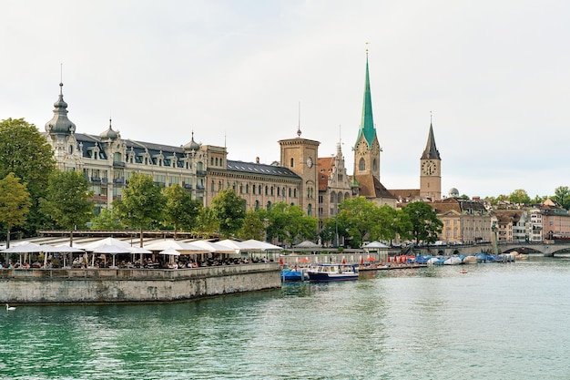 Zurych, Szwajcaria - 2 września 2016: Taras restauracji na nabrzeżu rzeki Limmat i kościół św. Piotra i kościół Fraumunster w centrum miasta Zurych, Szwajcaria.