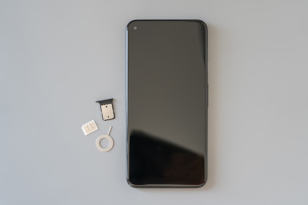 Zużyta karta Nano-SIM (4FF), tacka wyjęta ze slotu oraz ekstraktor do wyjęcia karty SIM i smartfona leżą na stole