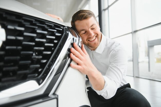 Zwiedzanie salonu samochodowego Przystojny brodaty mężczyzna głaszcze swój nowy samochód i uśmiecha się