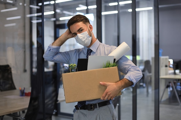 Zdjęcie zwolnienie pracownika w przypadku epidemii koronawirusa. zwolniony pracownik wychodzący z biura z materiałami biurowymi.